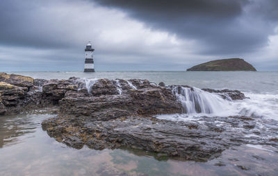 Lighthouse on rocks by sea against sky