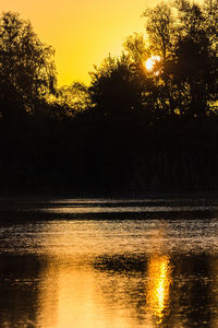 Silhouette trees by lake against sky during sunset