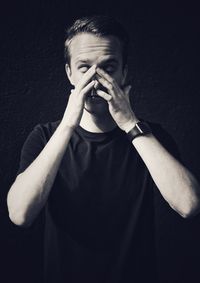 Portrait of young man covering face against black background