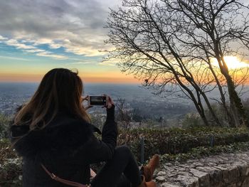 Midsection of woman photographing at sunset