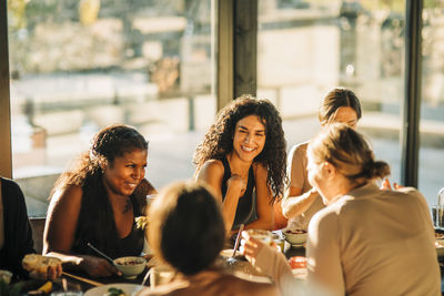 Cheerful female friends laughing while having breakfast together at retreat center