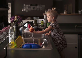 Side view of girl washing apple at kitchen sink