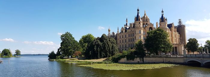 Panoramic view of buildings and trees by river against sky