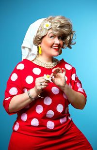 Cheerful woman stands with a flower on a blue background.