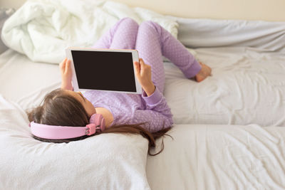 Girl with headphones watching digital tablet lying on bed at home