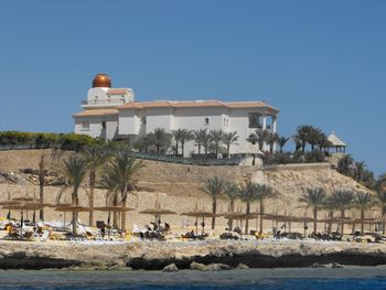 Buildings by sea against clear blue sky