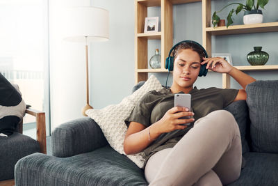 Full length of man using mobile phone while sitting on sofa at home