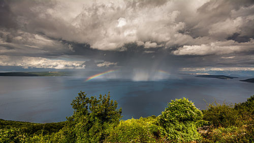 Scenic view of a full rainbow in front of krk island against dramatic sky over the deep blue ocean