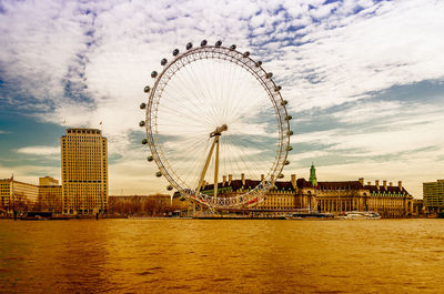 Ferris wheel in city against cloudy sky