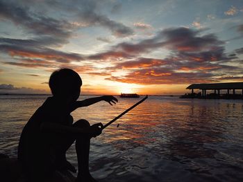 Silhouette woman by sea against sky during sunset