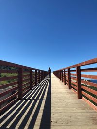 Rear view of woman walking on footbridge against sky