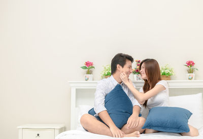 Mid adult couple sitting on bed against wall at home