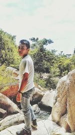 Boy standing on rock against sky