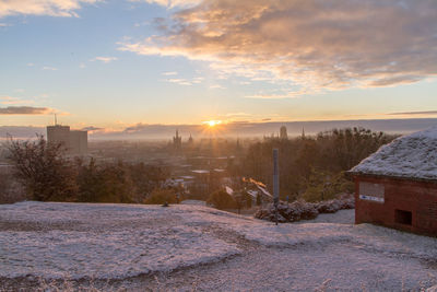 Snow covered cityscape against sky during sunset