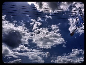 Low angle view of electricity pylon against cloudy sky