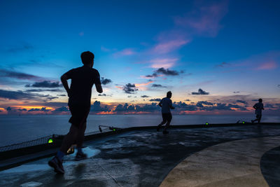 Silhouette people running against sky during sunset