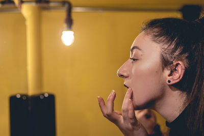 Side view of young woman against illuminated light bulb