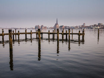 Wooden posts on lake by city against clear sky