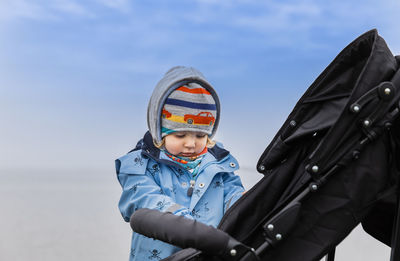 Cute baby girl standing wearing warm clothing while standing by carriage