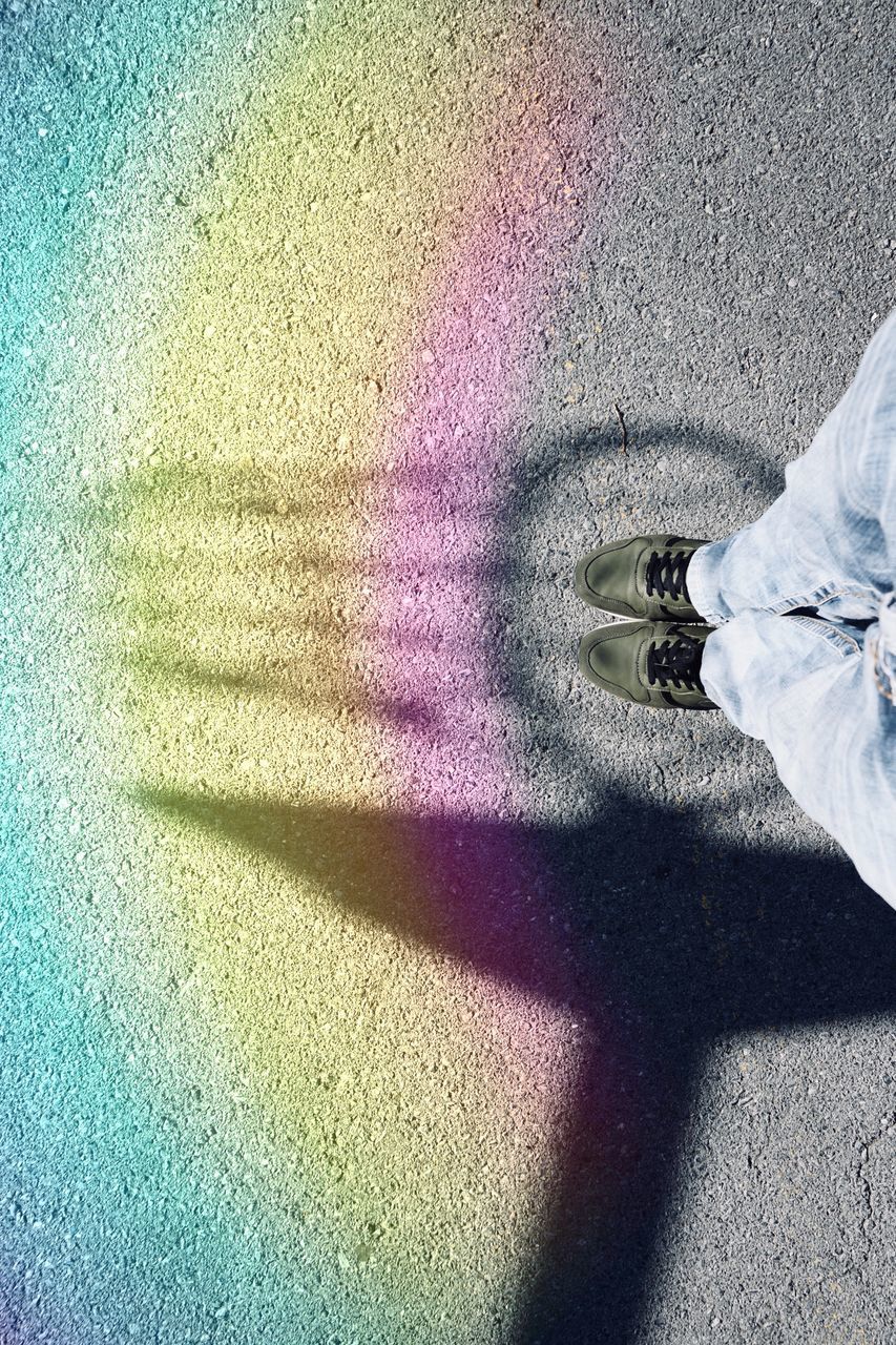 LOW SECTION OF PERSON STANDING ON MULTI COLORED SHADOW