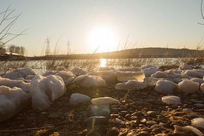 Rocks on snow covered land against sky during sunset