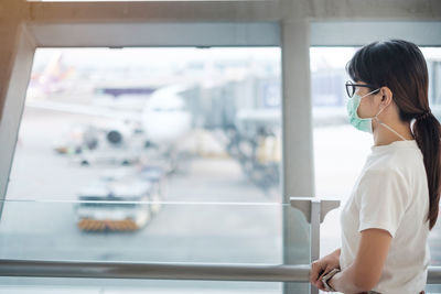 Side view of young woman looking through window