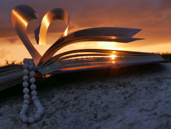 Book pages with beads making heart shape on rock during sunset