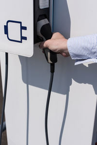 Cropped hand holding charger at electric vehicle charging station
