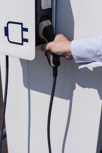 Cropped hand holding charger at electric vehicle charging station