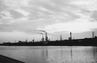 Factory by river against sky