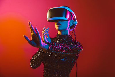 Young woman with shaved head wearing virtual reality glasses against orange background