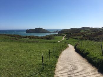 Footpath by sea against clear sky