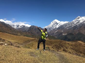 Man gesturing while standing on mountain against blue sky