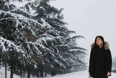 Young woman in fur coat standing by snowy trees against clear sky