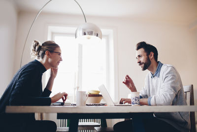 Side view of couple talking while sitting at dining table at home