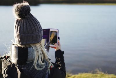 Rear view of woman photographing with mobile phone in river