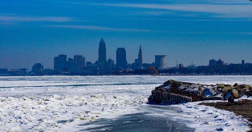 Scenic view of frozen sea by buildings against sky during winter