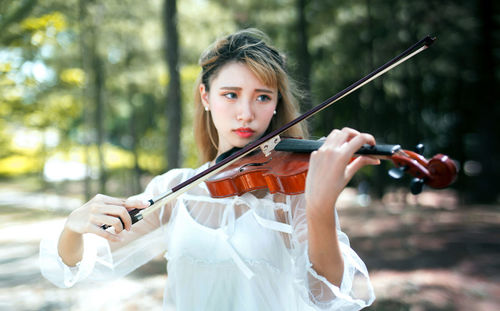 Young woman looking away while playing violin in park