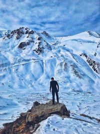 Rear view of man standing on rock while looking at snowcapped mountain