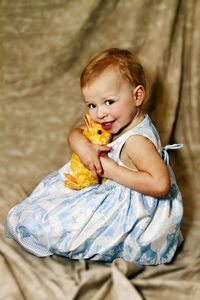 Portrait of cute baby girl holding stuffed toy while sitting on bed at home