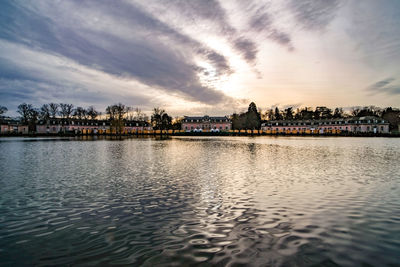 Scenic view of river by buildings against sky at sunset