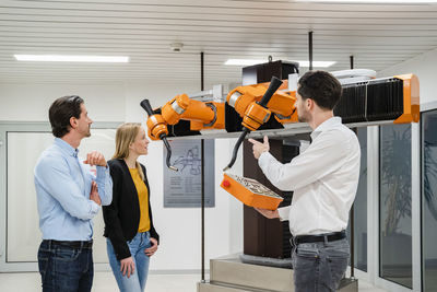 Technician operating robots near colleagues in factory