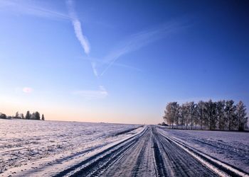 Snow covered street during winter against blue sky