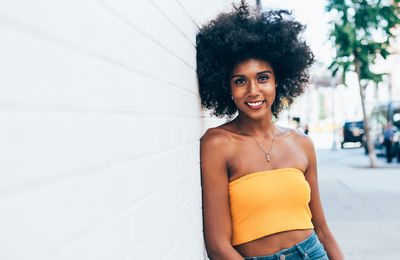 Portrait of happy young woman leaning on white wall in city