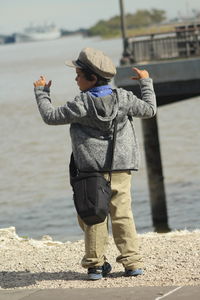 Rear view of boy gesturing while standing at beach