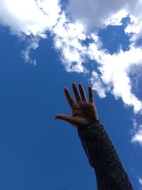 Low angle view of person hand against blue sky