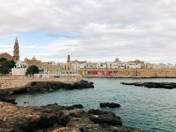 Buildings at waterfront against cloudy sky