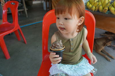 Close-up of cute girl holding ice cream while sitting on chair