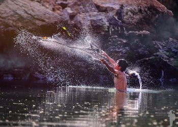 Shirtless fisherman casting fishing net in lake