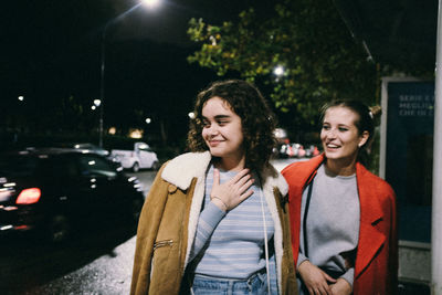 Portrait of smiling young woman standing on illuminated street at night